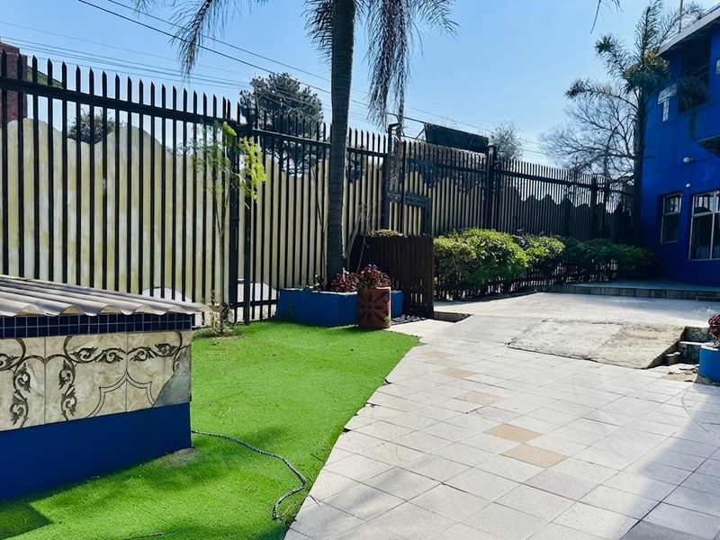 Rear exterior area featuring a paved walkway, artificial turf, and secure metal perimeter fencing with a decorative tiled feature wall.