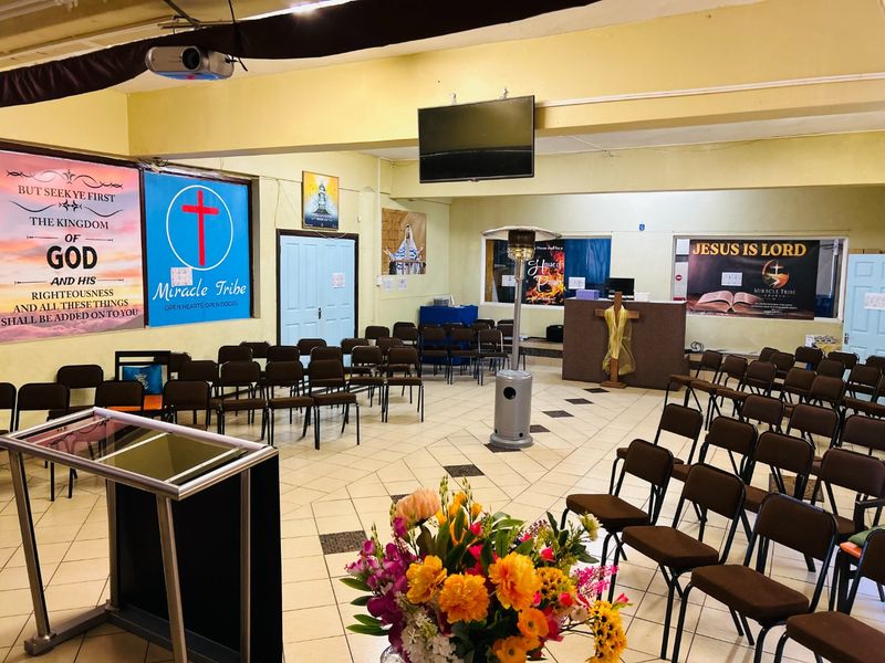 A large open-plan commercial hall currently used as a place of worship, featuring tiled flooring, a podium, and integrated audiovisual equipment.