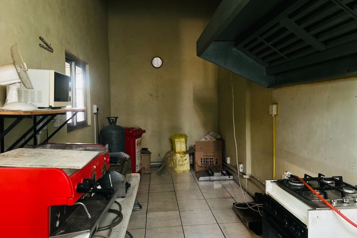 A commercial kitchen space featuring a gas stove, large extractor fan, and tiled flooring, currently showing signs of wear and dated wall finishes.