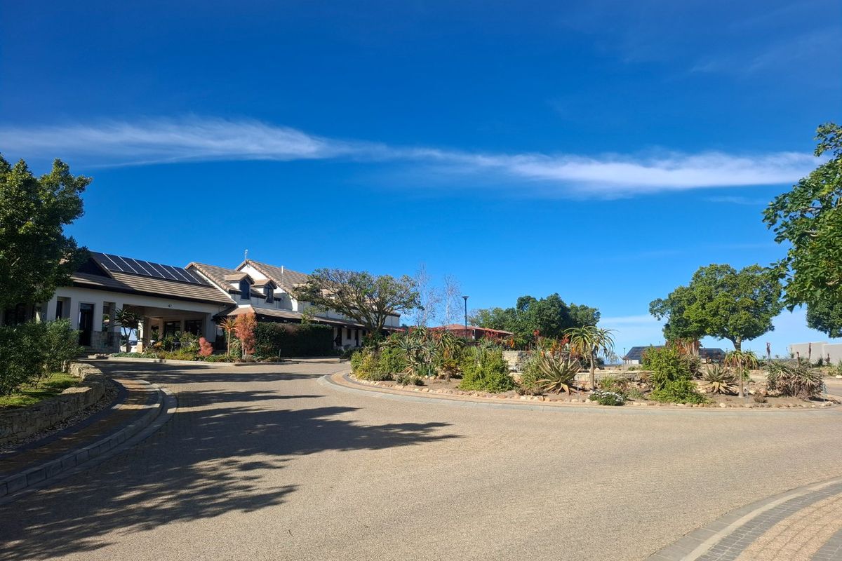 A well-maintained residential street view featuring a paved driveway, landscaped garden beds, and a building with roof-mounted solar panels under a clear sky.