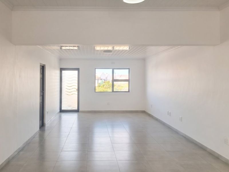 A bright, spacious, and empty living area featuring neutral tiled flooring, clean white walls, and modern aluminium window and door frames.