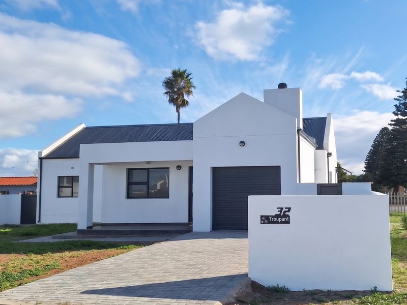 A modern, well-maintained single-story house featuring a paved driveway, single garage, and clean white exterior facade.
