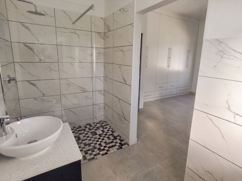 Modern bathroom featuring a walk-in shower with marble-look tiling, a vessel sink on a vanity, and adjacent built-in storage cabinetry.