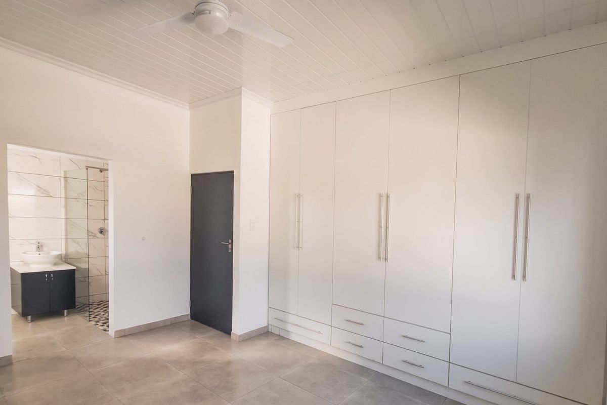 Spacious bedroom featuring extensive built-in cupboards, tiled flooring, a ceiling fan, and an adjoining en-suite bathroom with a modern vanity and shower.