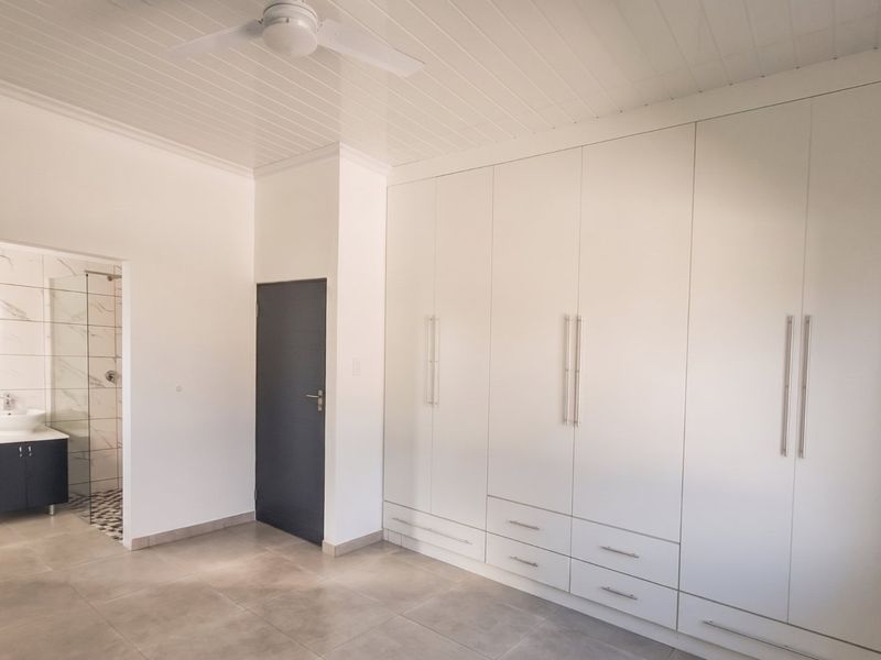 Spacious bedroom featuring extensive built-in cupboards, tiled flooring, a ceiling fan, and an adjoining en-suite bathroom with a modern vanity and shower.