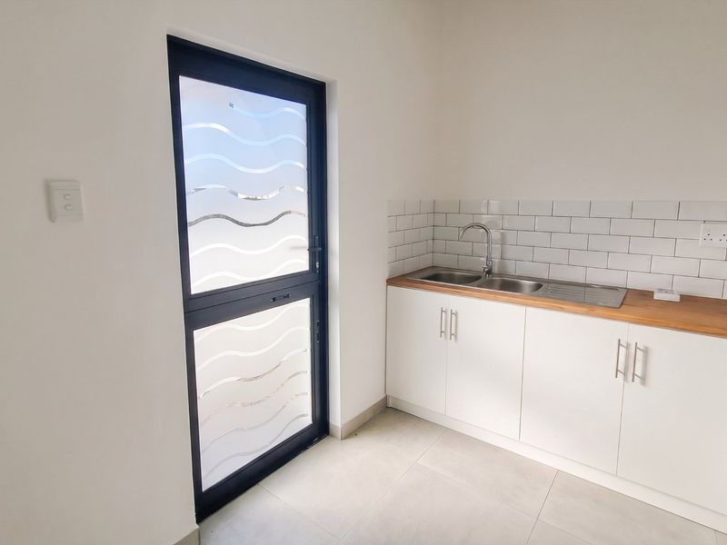 A clean, modern laundry area featuring built-in cabinetry, a wooden countertop with a stainless steel sink, and a frosted glass exterior door.
