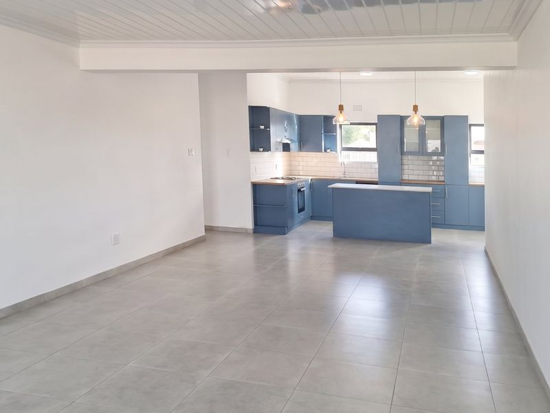 Spacious open-plan living area featuring a modern kitchen with blue cabinetry, subway tile backsplash, and tiled flooring throughout.