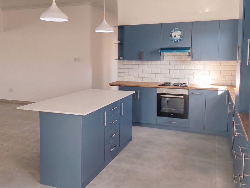 Modern open-plan kitchen featuring blue cabinetry, a central island with stone countertop, subway tile backsplash, and integrated stainless steel appliances.