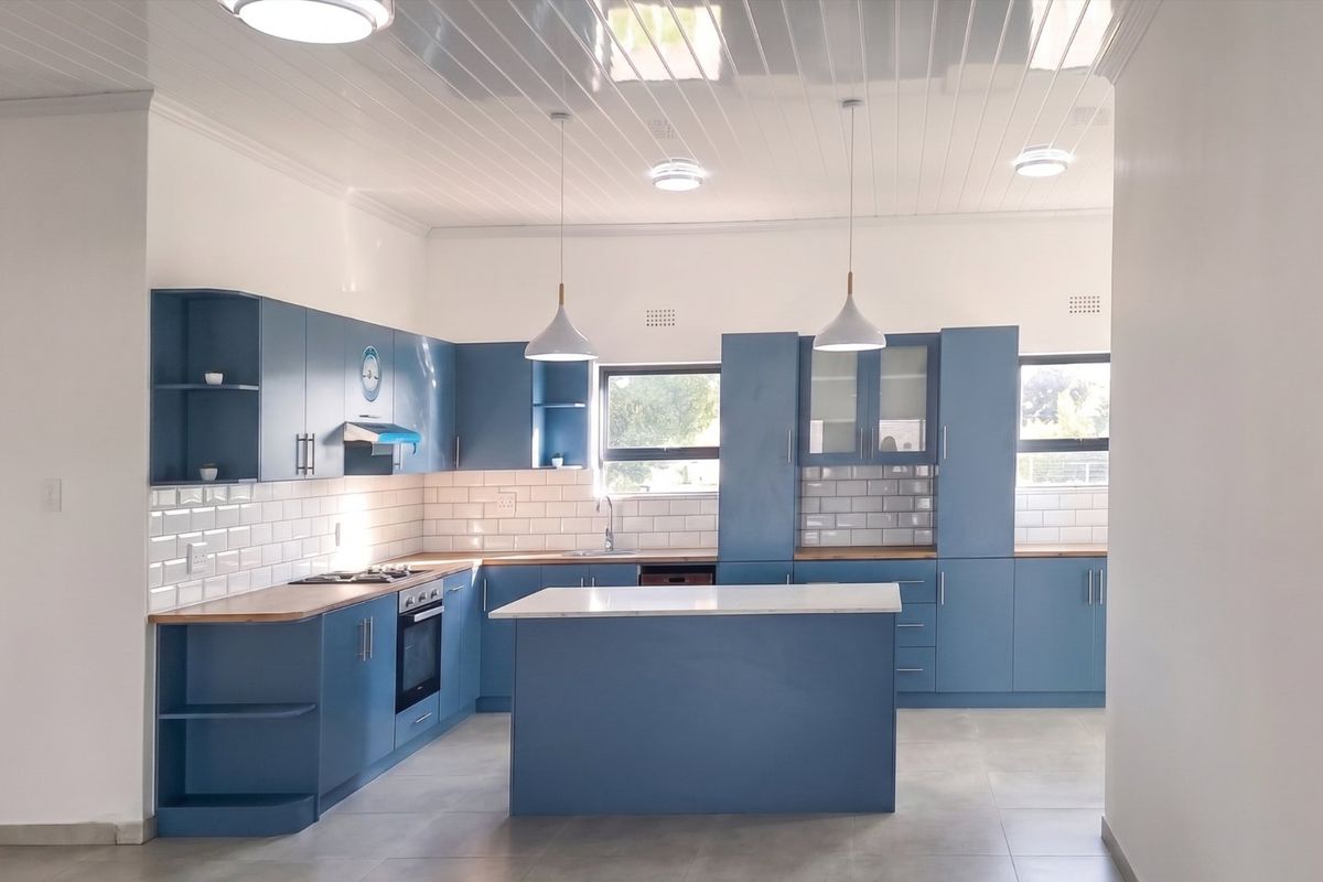 Modern kitchen featuring blue cabinetry, timber countertops, a central island, subway tile backsplash, and integrated appliances under a clean tongue and groove ceiling.