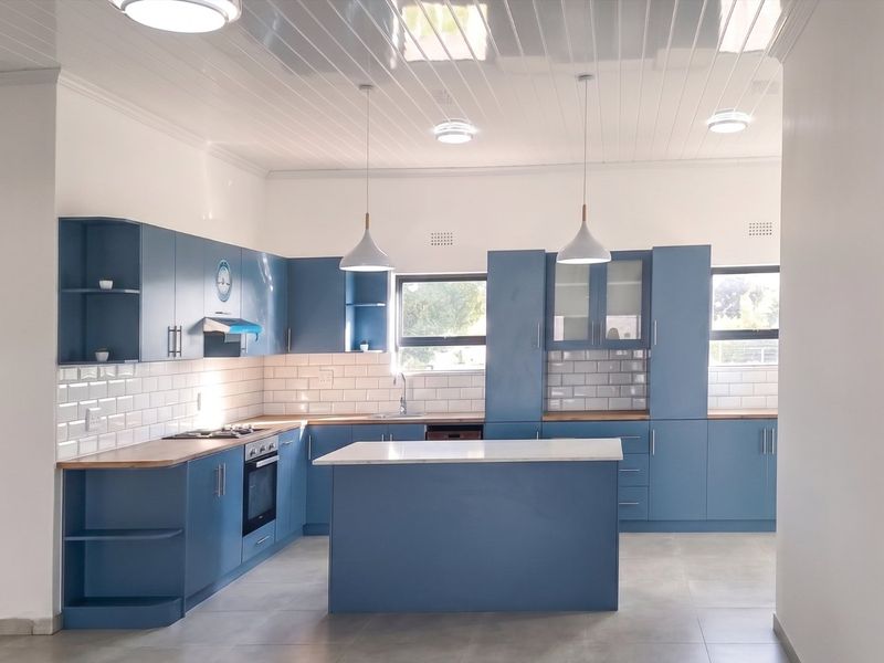 Modern kitchen featuring blue cabinetry, timber countertops, a central island, subway tile backsplash, and integrated appliances under a clean tongue and groove ceiling.