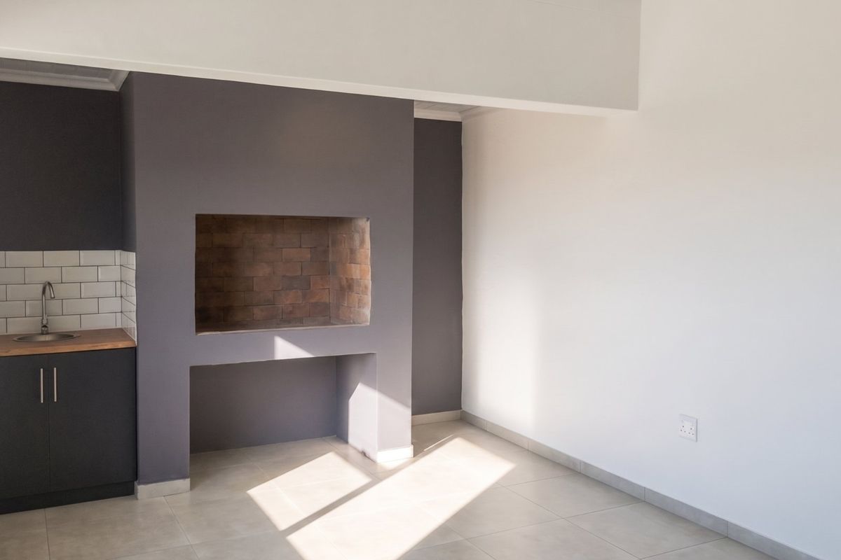A bright, open living area featuring a built-in fireplace and a convenient kitchenette corner with sink, cabinetry, and subway tile backsplash.