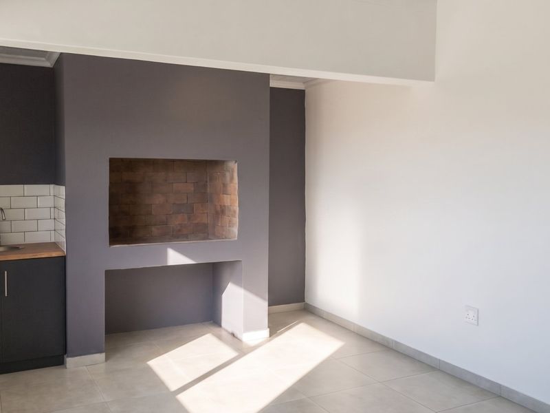 A bright, open living area featuring a built-in fireplace and a convenient kitchenette corner with sink, cabinetry, and subway tile backsplash.