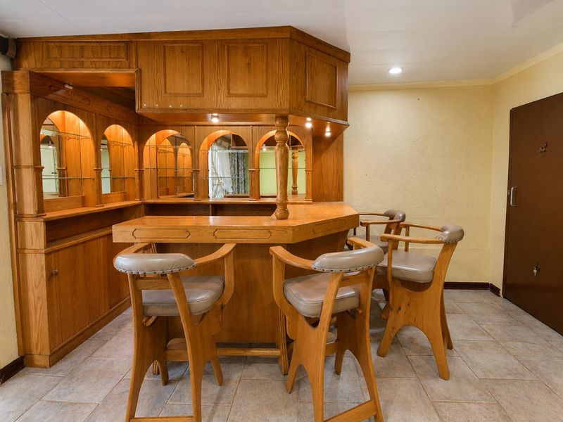 A dedicated bar area featuring custom built-in wooden cabinetry, integrated shelving, and tiled flooring, providing a classic entertainment space.