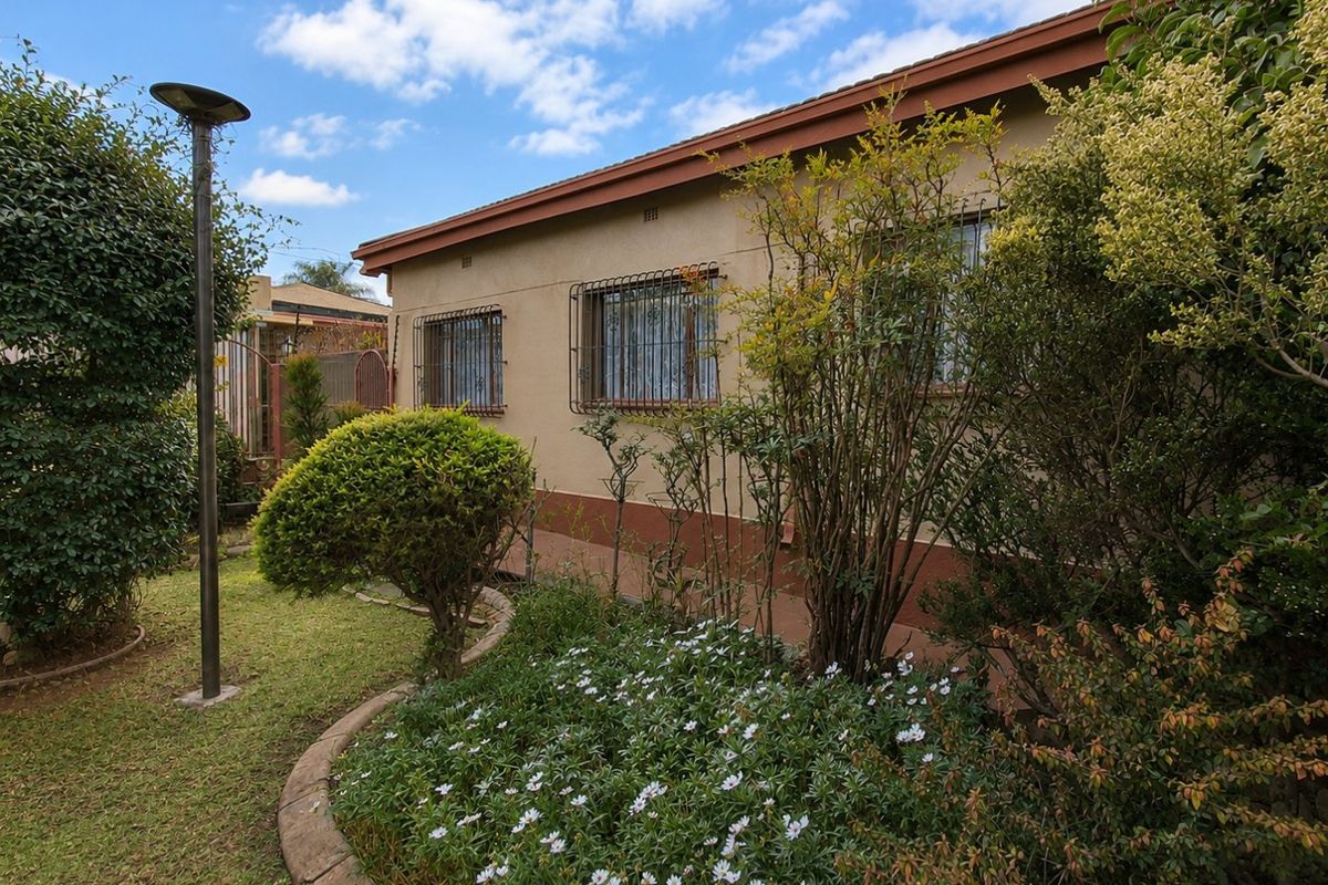 A view of the rear exterior of the house featuring a well-maintained garden with established landscaping and security bars on the windows.