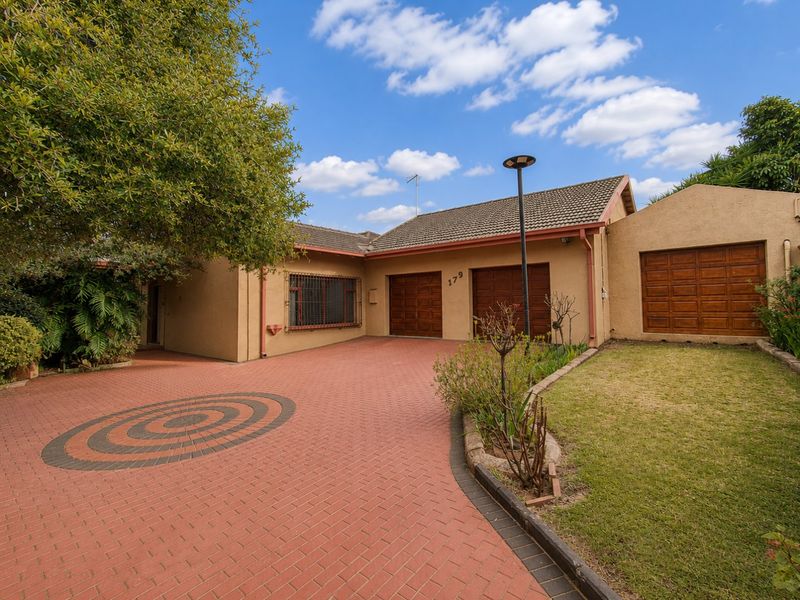 Front exterior view of a single-story house featuring a paved driveway, triple garage doors, and a well-maintained garden area.