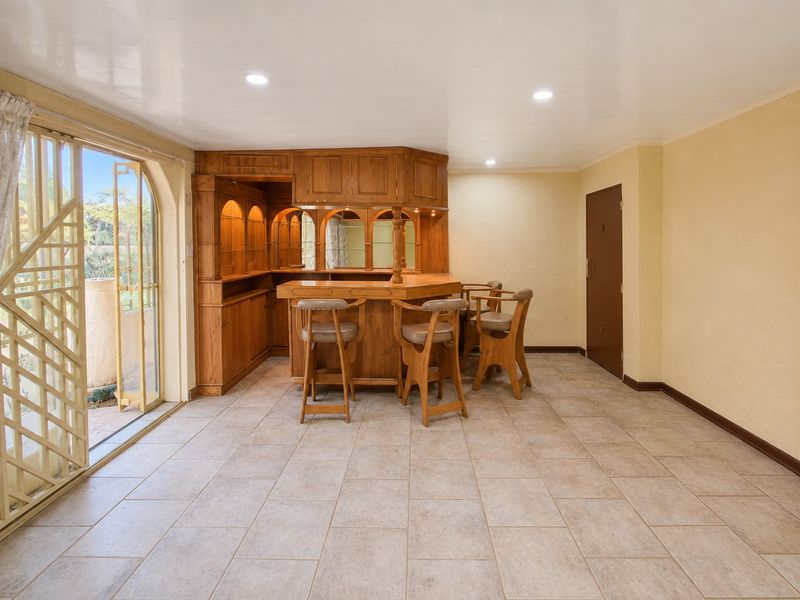 A dedicated bar area featuring a built-in wooden bar counter, tiled flooring, and direct access to the outdoor patio through a sliding glass door.