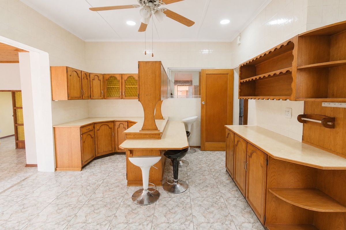 A spacious kitchen featuring traditional wooden cabinetry, laminate countertops, tiled flooring, and a central breakfast bar with integrated seating.
