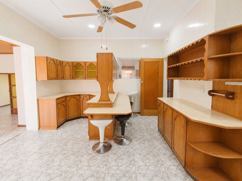 A spacious kitchen featuring traditional wooden cabinetry, laminate countertops, tiled flooring, and a central breakfast bar with integrated seating.