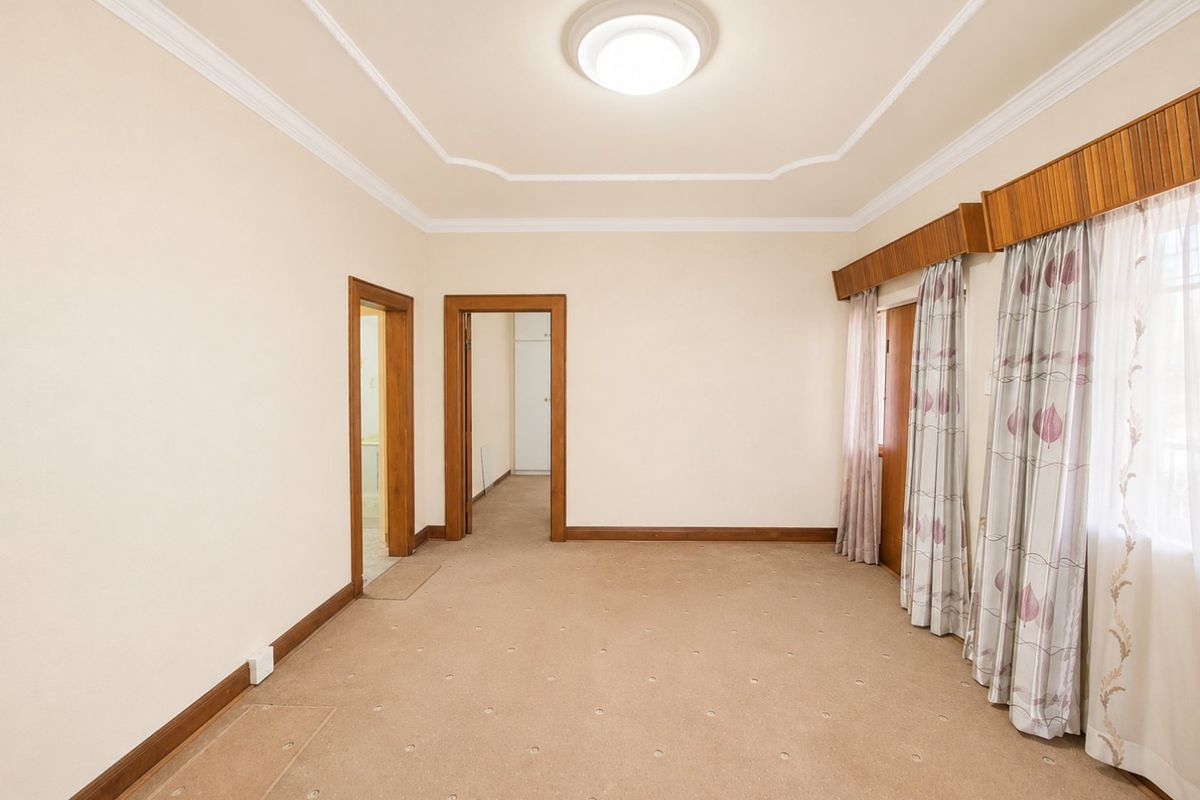 A spacious, empty bedroom featuring neutral walls, carpeted flooring, and classic timber trim details, offering a blank canvas for personalization.
