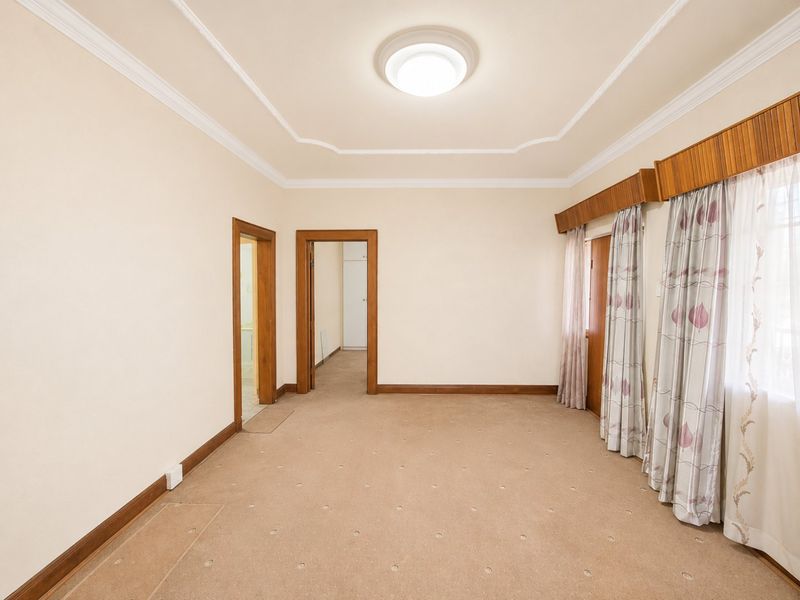 A spacious, empty bedroom featuring neutral walls, carpeted flooring, and classic timber trim details, offering a blank canvas for personalization.