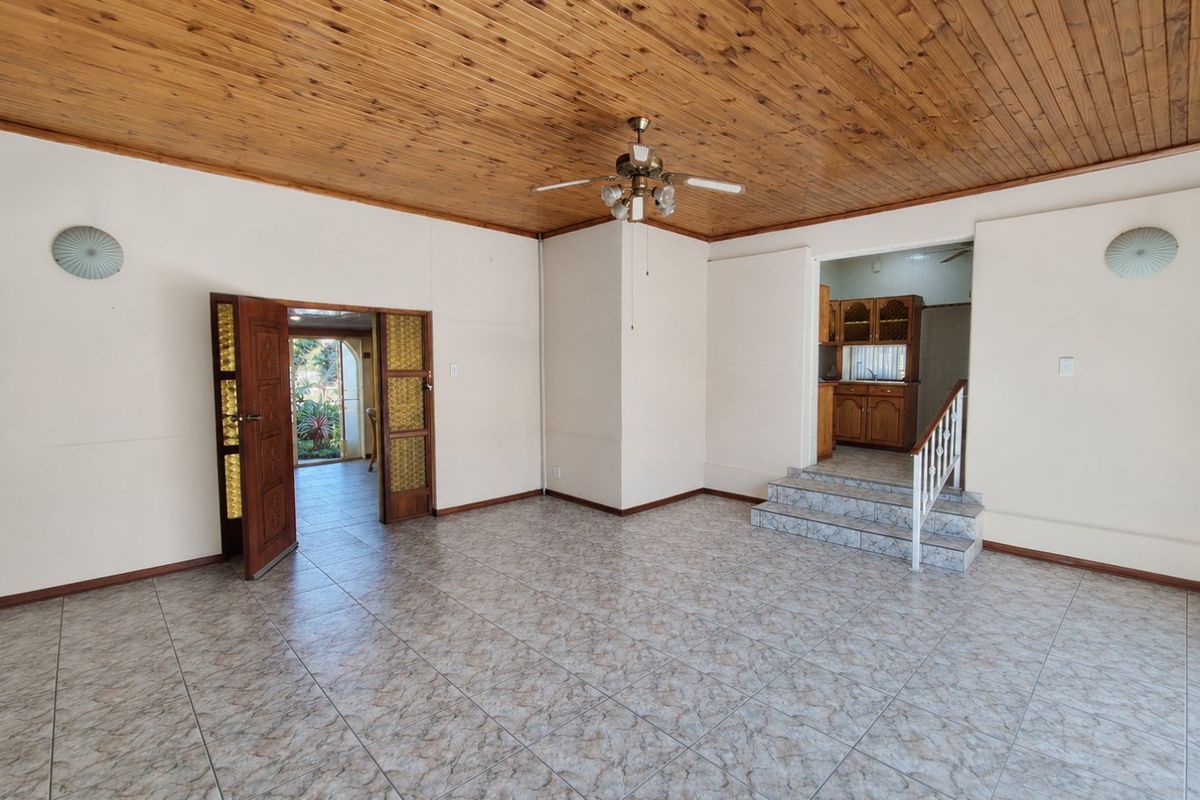Spacious living area featuring a timber ceiling, ceiling fan, and tiled flooring, with a staircase leading to an adjacent kitchen area.
