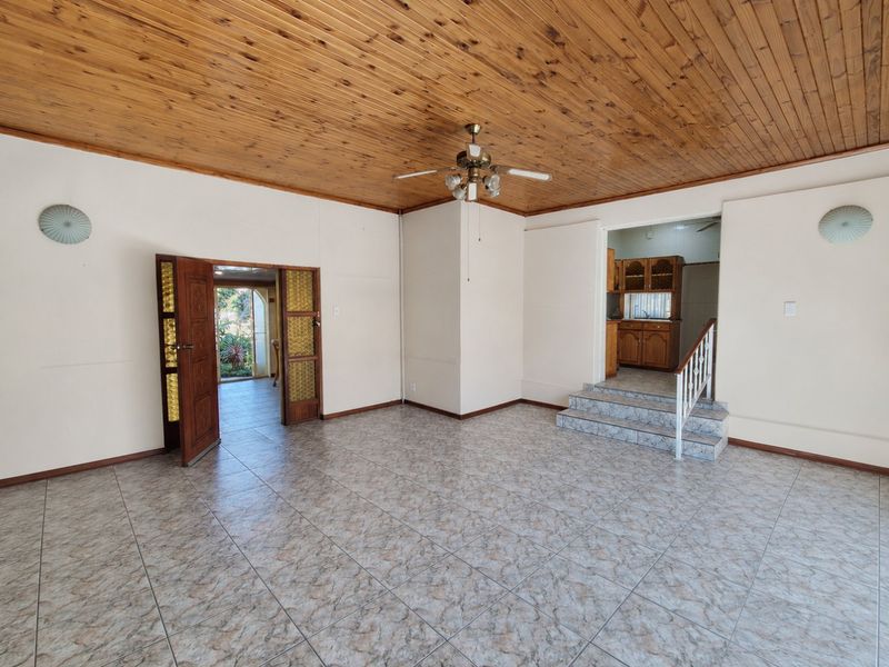 Spacious living area featuring a timber ceiling, ceiling fan, and tiled flooring, with a staircase leading to an adjacent kitchen area.