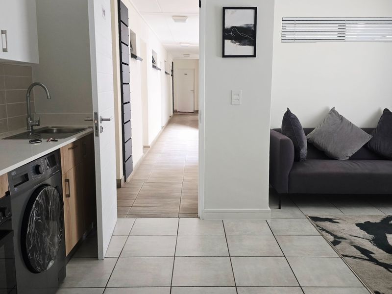 Open-plan living area featuring a modern kitchen with built-in appliances, tiled flooring, and direct access to an internal hallway.