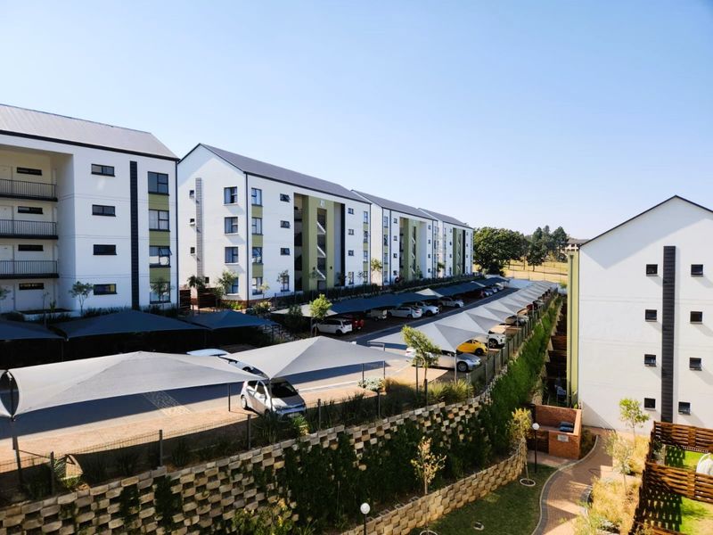 Aerial view of a modern apartment complex featuring multi-story residential blocks, extensive shade-cloth covered parking, and landscaped retaining walls.
