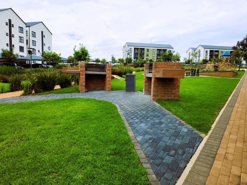 A well-maintained communal garden area featuring brick braai facilities, paved walkways, and landscaped lawns within an apartment complex.