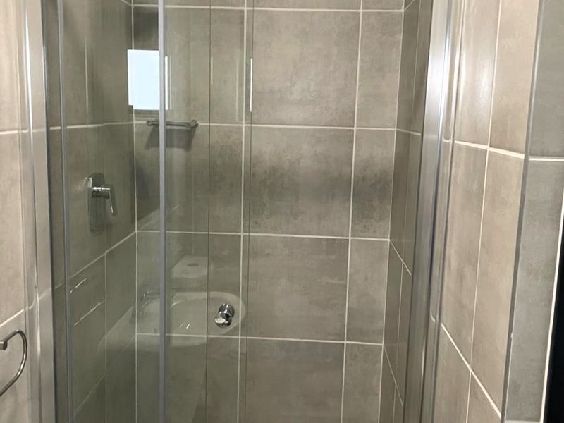A modern bathroom shower enclosure featuring neutral grey ceramic wall and floor tiles with a sliding glass door and chrome shower fixtures.