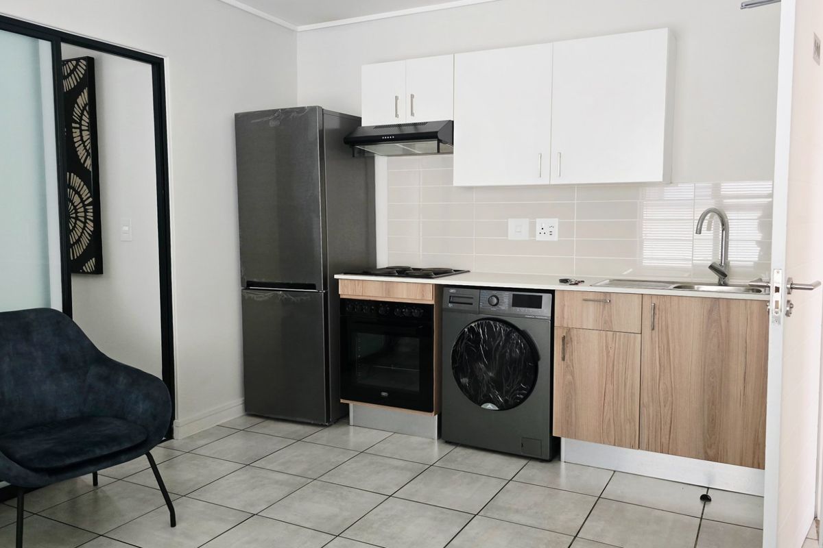 Compact modern kitchen featuring built-in cabinetry, integrated oven and hob, extractor fan, and tiled backsplash with neutral finishes.