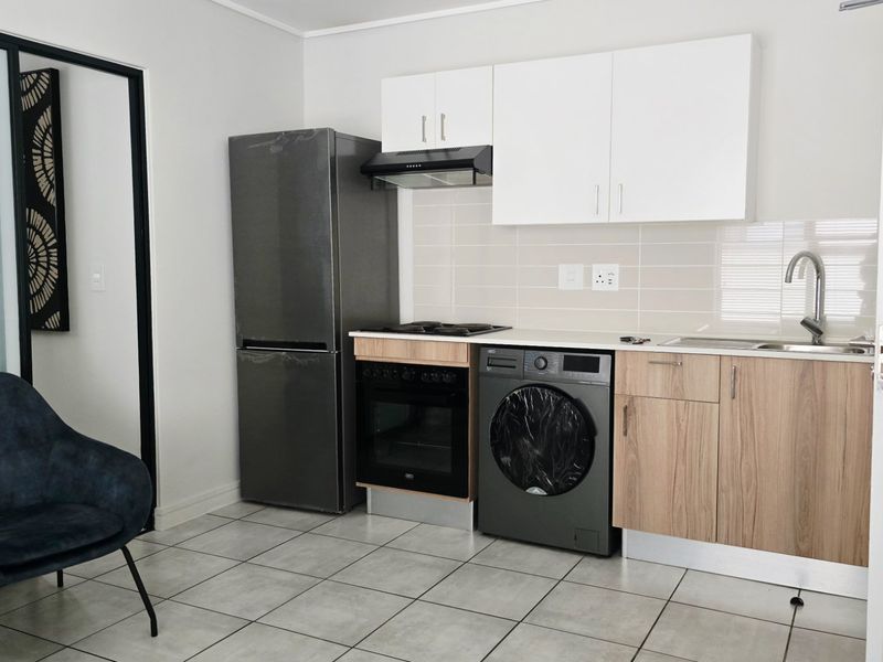 Compact modern kitchen featuring built-in cabinetry, integrated oven and hob, extractor fan, and tiled backsplash with neutral finishes.