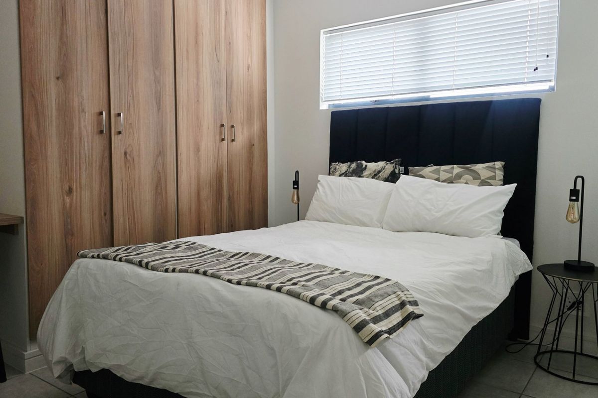A well-maintained bedroom featuring modern wood-finish built-in cupboards, tiled flooring, and a window fitted with venetian blinds.