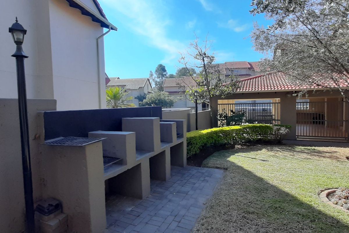 Rear garden area featuring a paved patio with a built-in braai, landscaped lawn, and access to a covered carport.