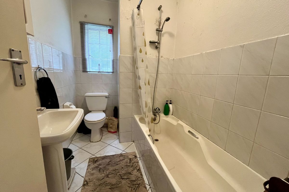 A functional bathroom featuring a pedestal basin, toilet, and a bathtub with a shower mixer, finished with tiled walls and flooring.