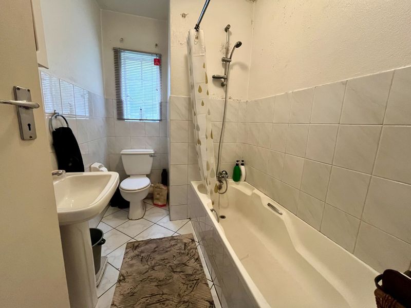 A functional bathroom featuring a pedestal basin, toilet, and a bathtub with a shower mixer, finished with tiled walls and flooring.