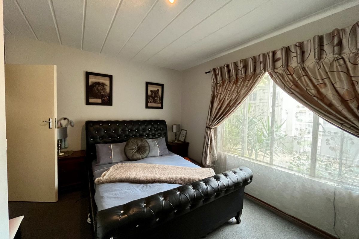 A bedroom featuring carpeted flooring, a panelled ceiling, and a window fitted with security bars.