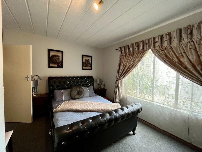 A bedroom featuring carpeted flooring, a panelled ceiling, and a window fitted with security bars.