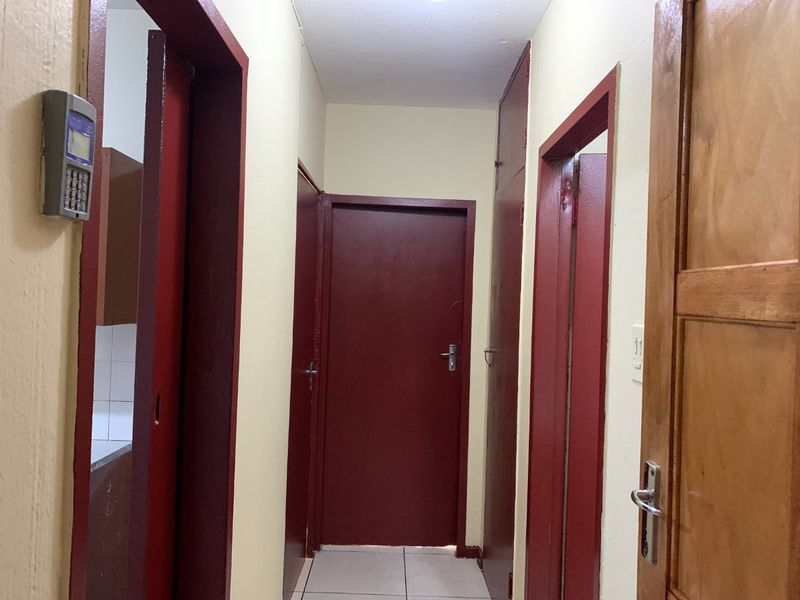 A functional hallway featuring tiled flooring and multiple internal doors with a wall-mounted security keypad.