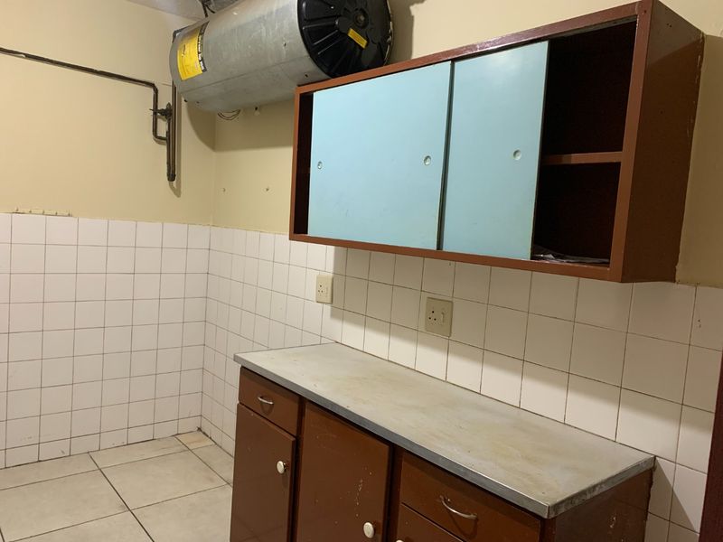 A functional laundry area featuring built-in cabinetry, a metal countertop, tiled splashback, and an installed electric water heater.