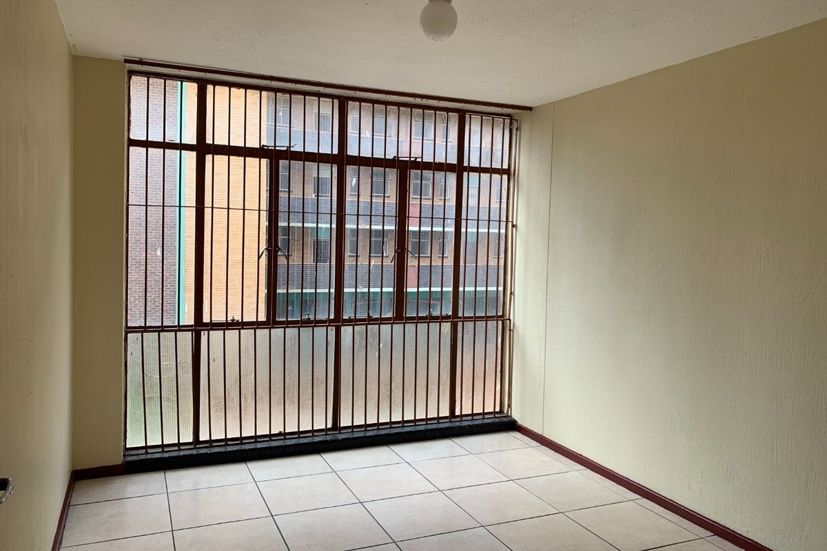 An empty living area featuring tiled flooring and large windows fitted with security bars, offering a blank canvas for renovation.