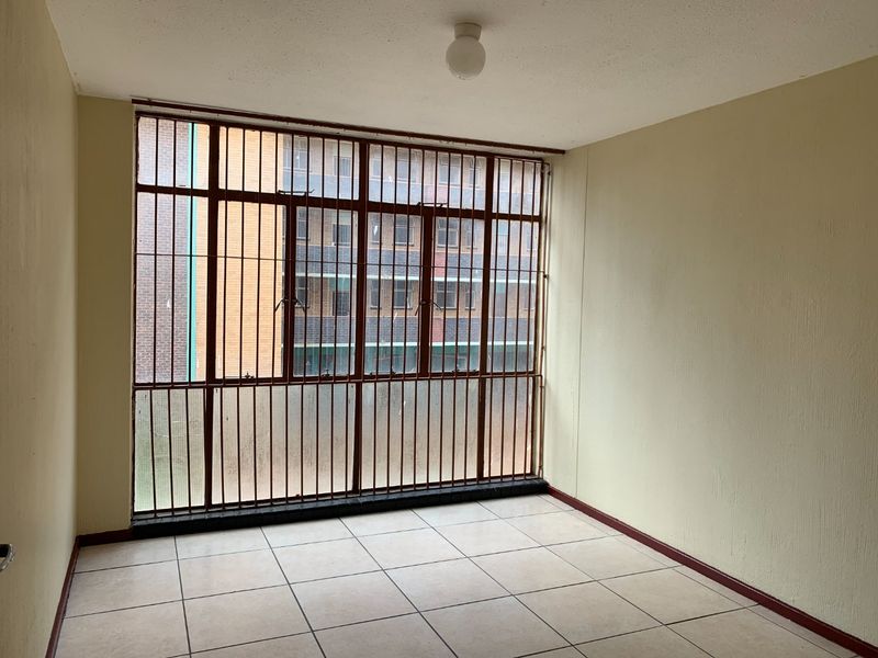 An empty living area featuring tiled flooring and large windows fitted with security bars, offering a blank canvas for renovation.