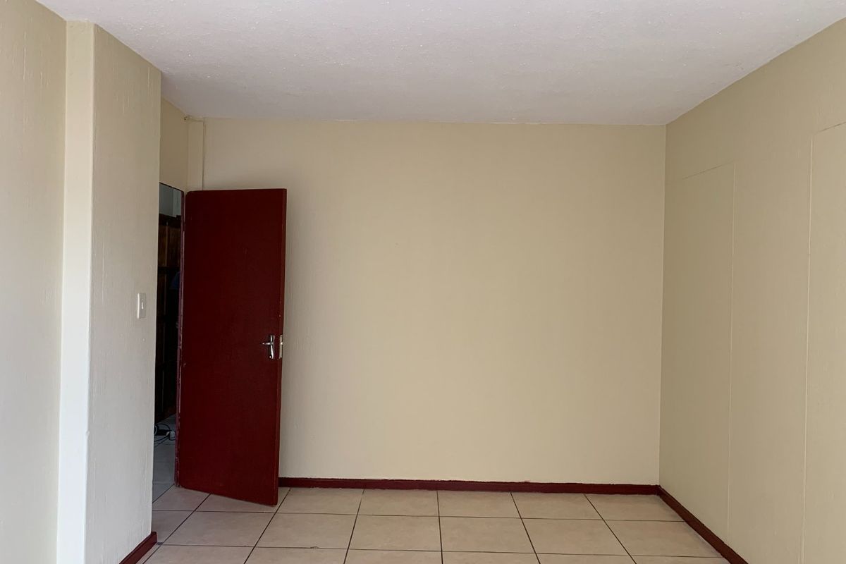 An empty bedroom featuring neutral wall paint, tiled flooring, and a contrasting red internal door.
