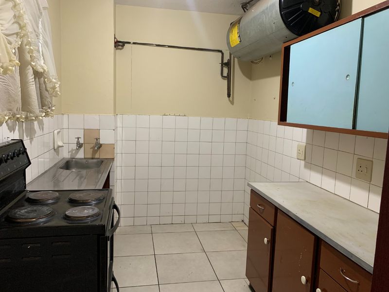 A dated kitchen featuring tiled splashbacks, built-in cabinetry, a stainless steel sink, and an electric stove, with an exposed geyser unit.