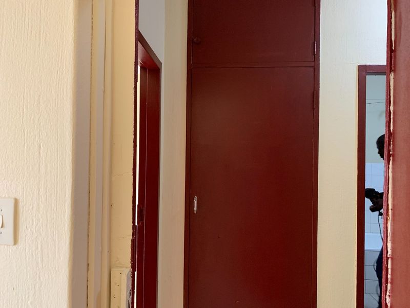 A narrow hallway featuring a built-in storage cupboard with a red painted finish and visible wear on the surrounding door frames.
