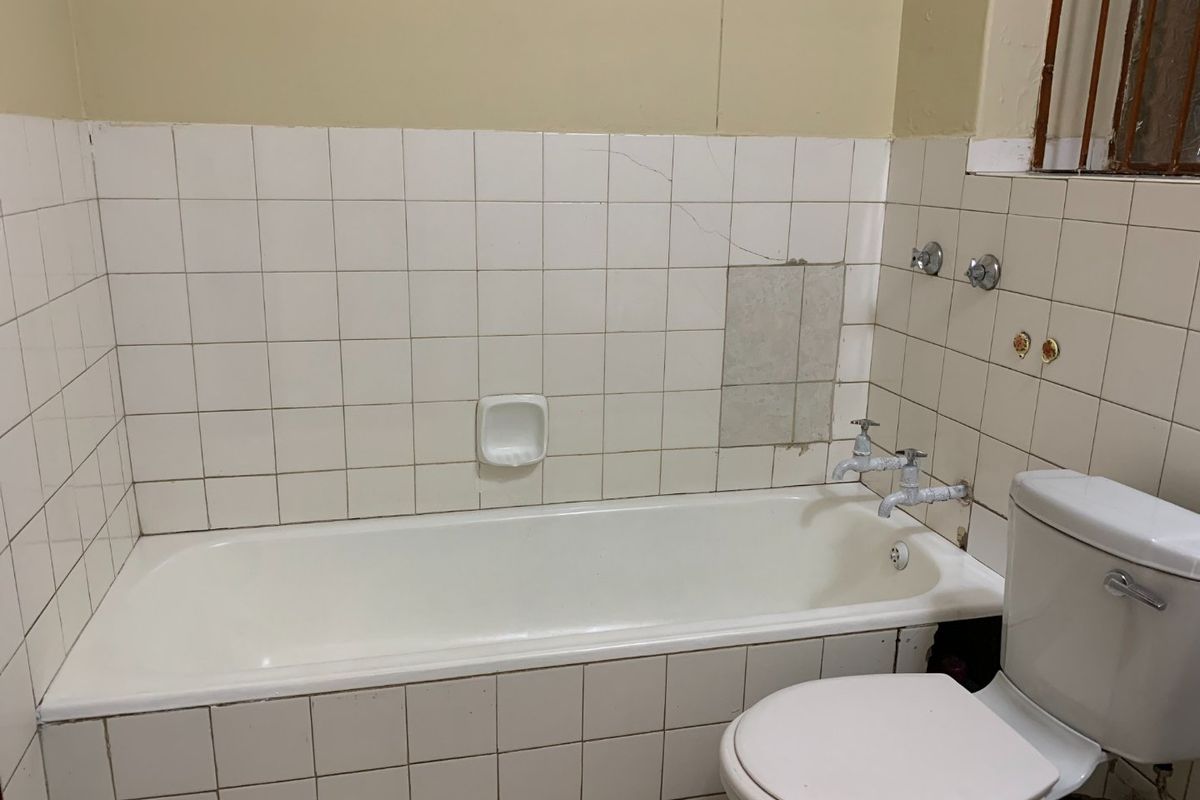 A dated bathroom featuring a standard bathtub and toilet with visible tile damage and worn plumbing fixtures, offering significant potential for renovation.