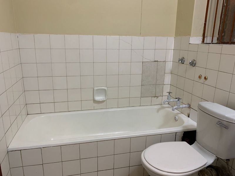 A dated bathroom featuring a standard bathtub and toilet with visible tile damage and worn plumbing fixtures, offering significant potential for renovation.