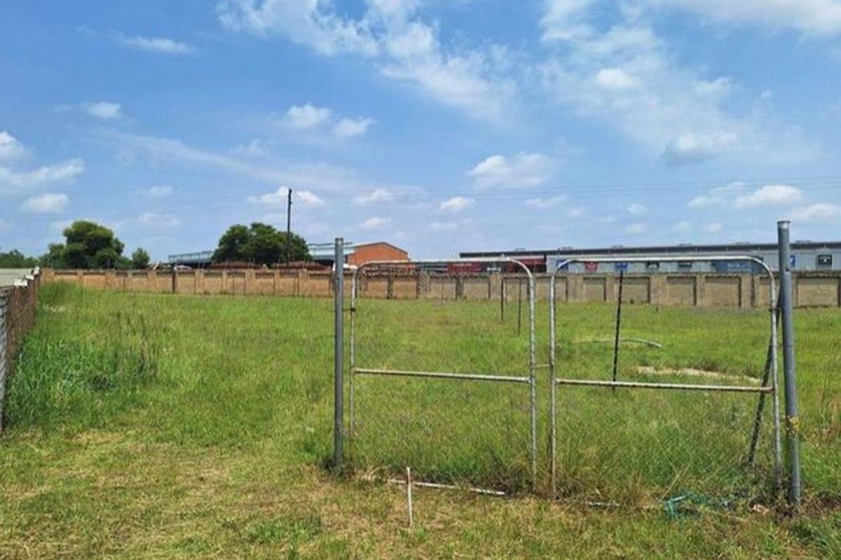 A vacant residential plot featuring perimeter brick walling, chain-link fencing, and a metal access gate, ready for development.