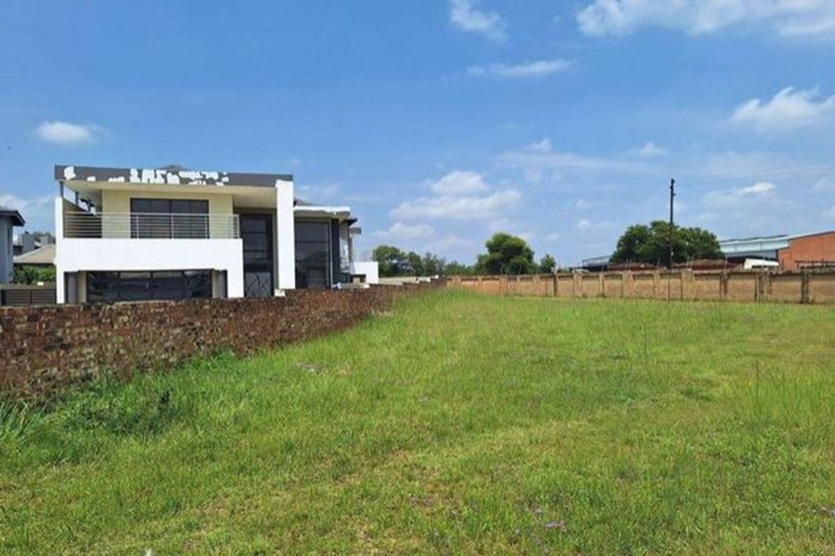 A vacant residential plot featuring a grass lawn, enclosed by a brick boundary wall and perimeter fencing, adjacent to an existing residential property.
