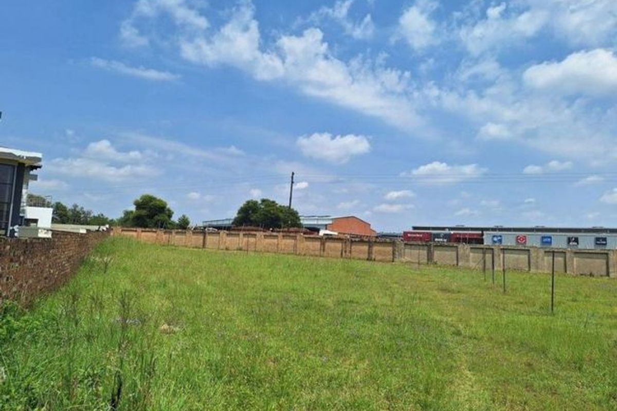 A vacant residential plot featuring a grassy landscape enclosed by a perimeter brick wall and fencing.